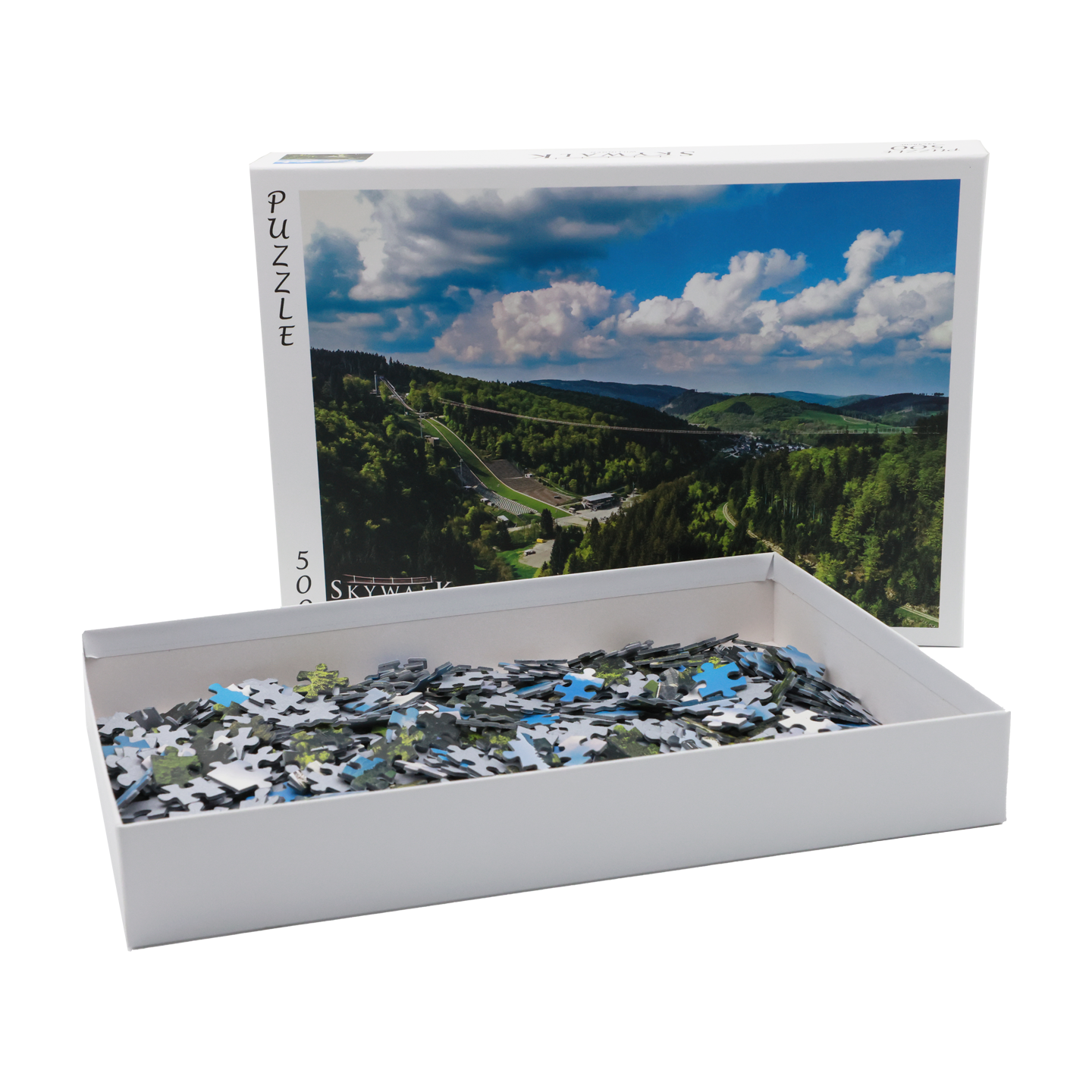 Bild: Das Bild zeigt die geöffnete Schachtel des Puzzles. Der Kartondekcel mit dem Motivbild steht dort hinter. Man sieht die Puzzleteile.