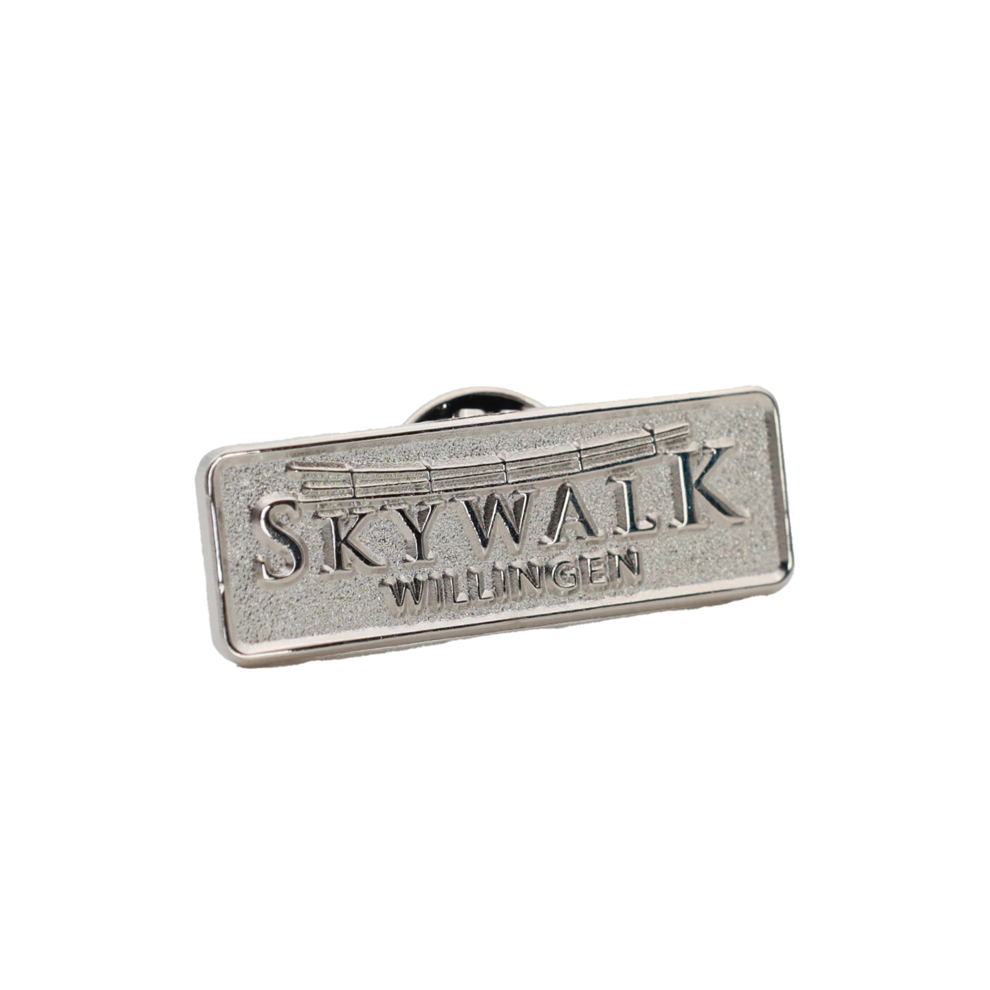 Bild: Es zeigt den Metallpin von vorne er ist naturbelassen silber. Das Motiv ist das Logo Skywalk-Willingen in hochglanz. Der Pin ist echteckig und hat abgerundete Kanten. Der Hintergrund des Logos ist angeraut. So setzten sich das Logo und der Rand nicht nur durch die unterschiedliche Höhe vom angerauten Hintergrund ab.  