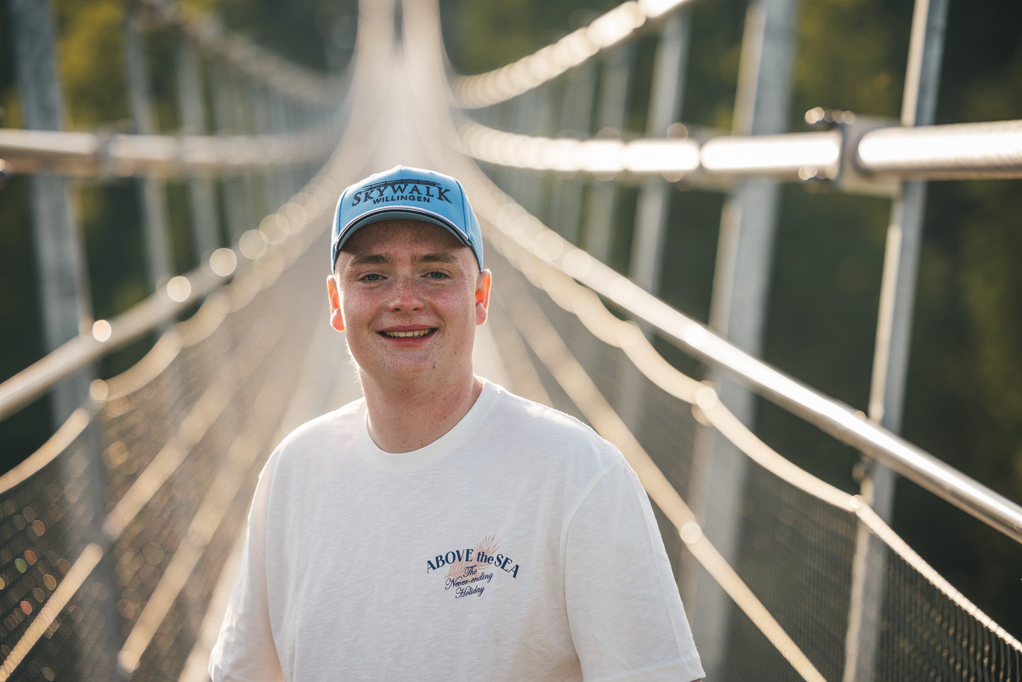 Bild: Es zeigt einen jungen Mann mit der Kappe von vorne. Er lächelt und steht auf dem Skywalk-Willingen.