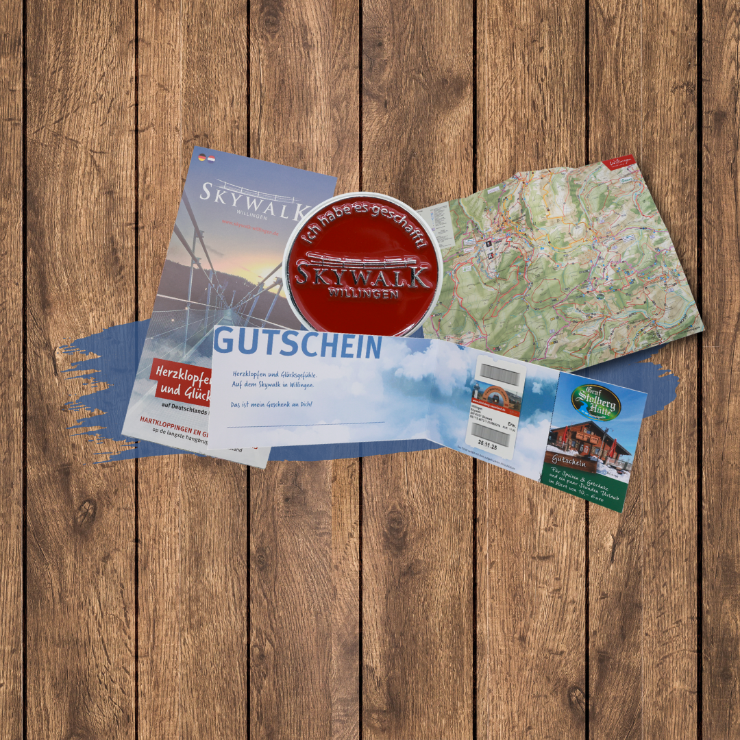 Bild 1 von 7: Zu sehen sind die einzelnen Produkte, die im Wanderpaket enthalten sind. Dies sind der runde rote Pin mit dem Skywalklogo und dem Spruch: "Ich habs geschafft", eine Wanderkarte der Region Willingen, ein Flyer vom Skywalk und ein aufgeklappter Gutschein mit dem Ticket für den Skywalk und dem Verzehrgutschein über 10 € der Graf Stolberg Hütte.